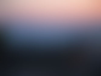 Person with hat and backpack overlooks a city at sunset. Sky is pink and orange, city lights twinkle, and silhouettes of hills are visible.