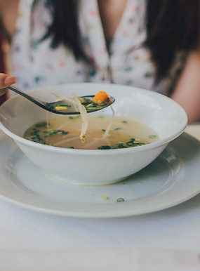 Picture showing a blurry female figure in the background holding a spoon atop a bowl of soup with beansprouts in the foreground