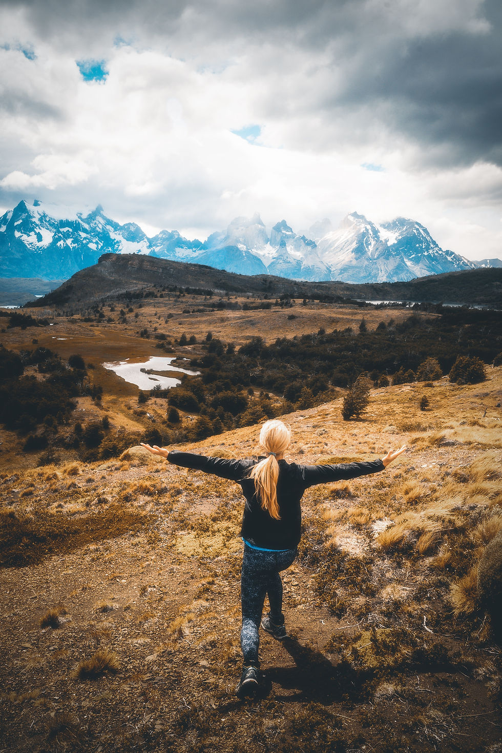 A traveler embraces the vast and breathtaking landscapes of Patagonia, Chile, with the iconic mountains under a dramatic sky.