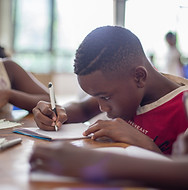A boy, focused on his writing, sitting at a table