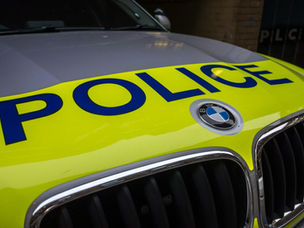 Close-up of a police car hood with "POLICE" in bold blue letters on a bright yellow background, featuring a BMW emblem.