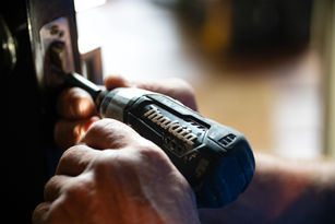 Hands using a power drill to fix a lock, set in a dimly lit room. Focus on tool brand, showcasing precision work.