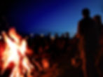 A large bonfire at the beach with a large group of people around