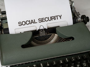 A vintage typewriter types "SOCIAL SECURITY" on white paper. The machine is green, set on a marble surface, conveying a retro vibe.