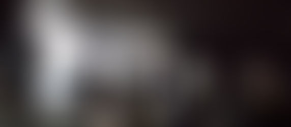 Film crew in a dimly lit studio, setting up equipment and monitors. Cables and spotlights surround them, creating a busy, focused atmosphere.