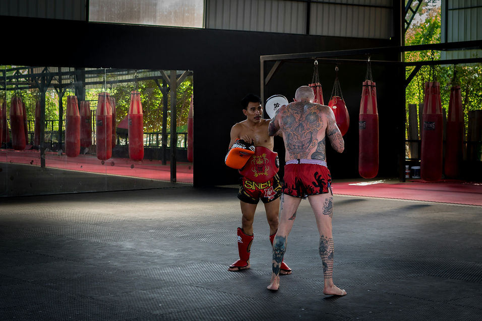 Fighters training in an outdoor Muay Thai gym surrounded by red ropes and sandbags.