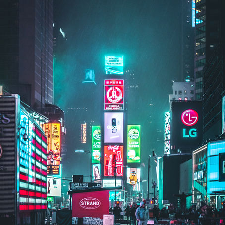 Neon-lit Times Square at night, featuring vibrant ads and logos. Rain-soaked pavement, people walking, and a moody, bustling atmosphere.