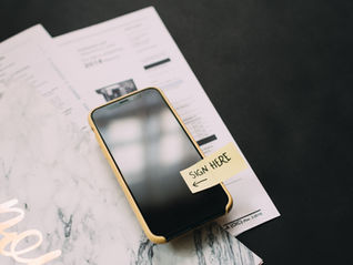 A cell phone with a "Sign Here" post-it attached to it.