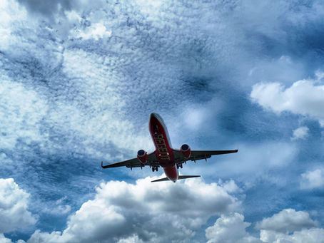 Passenger airplane flying overhead against a blue sky with scattered white clouds, showing the underside of the aircraft during ascent.