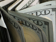 Close-up of folded U.S. $100 bills, showing blue security patterns and large 100 numerals in a tight stack.
