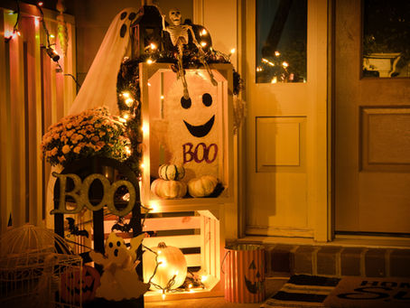 Festive porch decorated for Halloween with pumpkins, a ghost sign reading “BOO,” skeleton, fairy lights, and flowers by a warmly lit door — part of Stress-Free Halloween Tips by Neat Nathalie & Co.