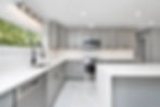 Modern kitchen with gray cabinets, white countertops, and tiled backsplash. Stainless steel appliances and large window with greenery outside.
