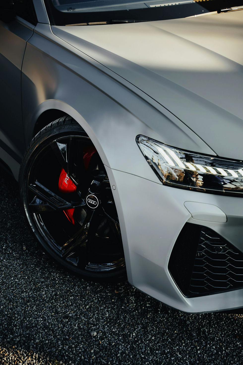Close-up of a gray Audi car's front wheel and headlight with black and red detailing.