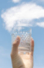 Clear water glass being held up to the sky.