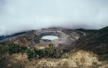 Cratere fumante del vulcano Poás in Costa Rica, avvolto da una nebbia misteriosa.
