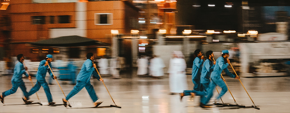 Six men sweeping the floor at a hurried pace.