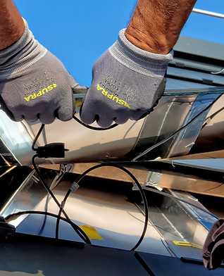 Techniker in Schutzhandschuhen montiert Verkabelung einer Solarpanel-Installation unter blauem Himmel