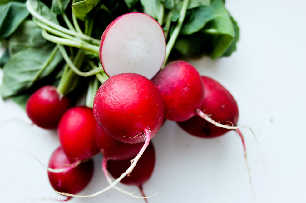 Red radishes with green leaves on a white background, one radish sliced to show the white interior. Bright colors, fresh appearance.
