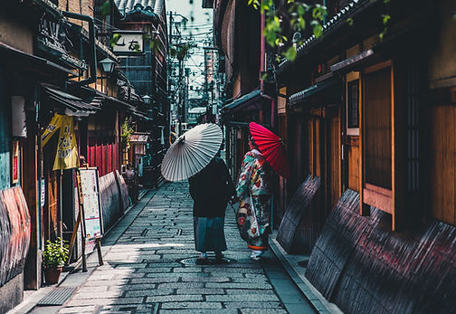 A couple wearing kimono and carrying paper umbrellas walk down a traditional Japanese street