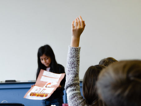 A student raising their hand while a teacher looks down