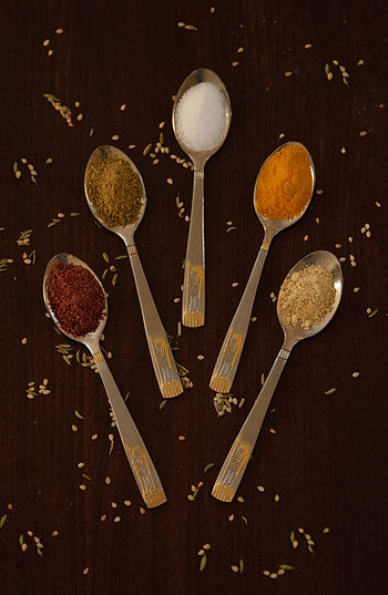 5 spoons with 5 different spices on each, representing the 5 primary flavors on a black background