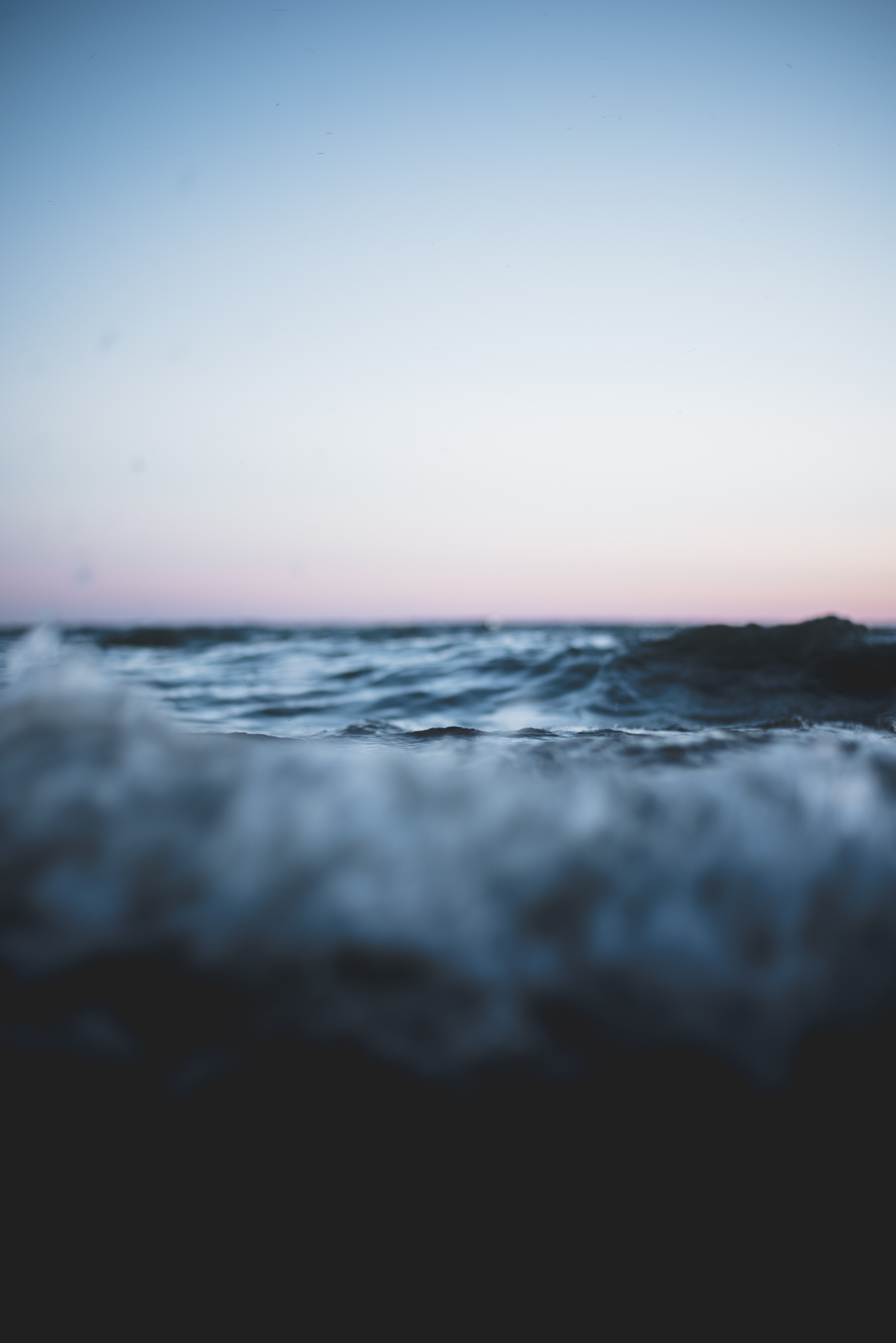 close up of dark blue gray ocean with a soft pink and blue sky in the background