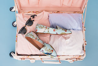Woman's open suitcase packed with clothes, shoes, and sunglasses