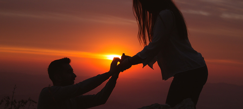 Un couple se faisant une demande en mariage, en silhouette sur fond de coucher de soleil chaleureux.