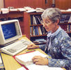 elderly lady working in the office with glass and grey hair wearing a blue and white dress