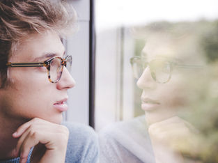 Man looking out of the window, we see his reflection in the glass.
