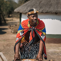 Man in traditional Zulu attire near a thatched hut