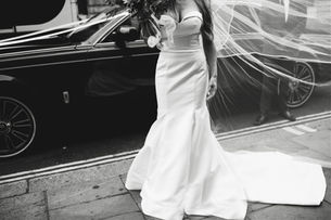 A high-quality editorial photograph of a bride stepping out of a pristine luxury sedan.