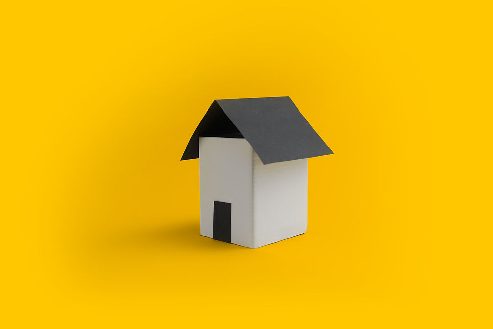 A small model house with a black roof and door sits against a bright yellow background, creating a minimalistic and contrasting scene.