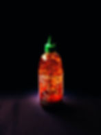 Bottle of sriracha that is nearly empty with a spotlight on the bottle to illuminate it against a black background. This is just one type of hot sauce to use for when you travel from home via at-home travel activities.