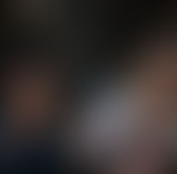 Two women sit together eating from bowls with chopsticks. They are focused on their meals. The background is dimly lit.