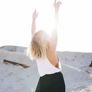 Arms thrown in the air with liberation and joy as the light shines on the traveller with blonde hair and white top