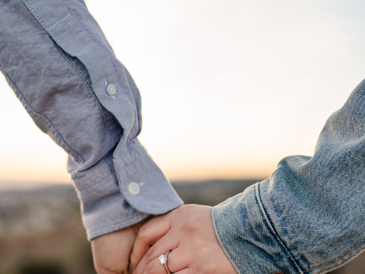 holding hands in the sun with the view focusing on the couple hands with the women's finger adorned with a single stone engagement ring