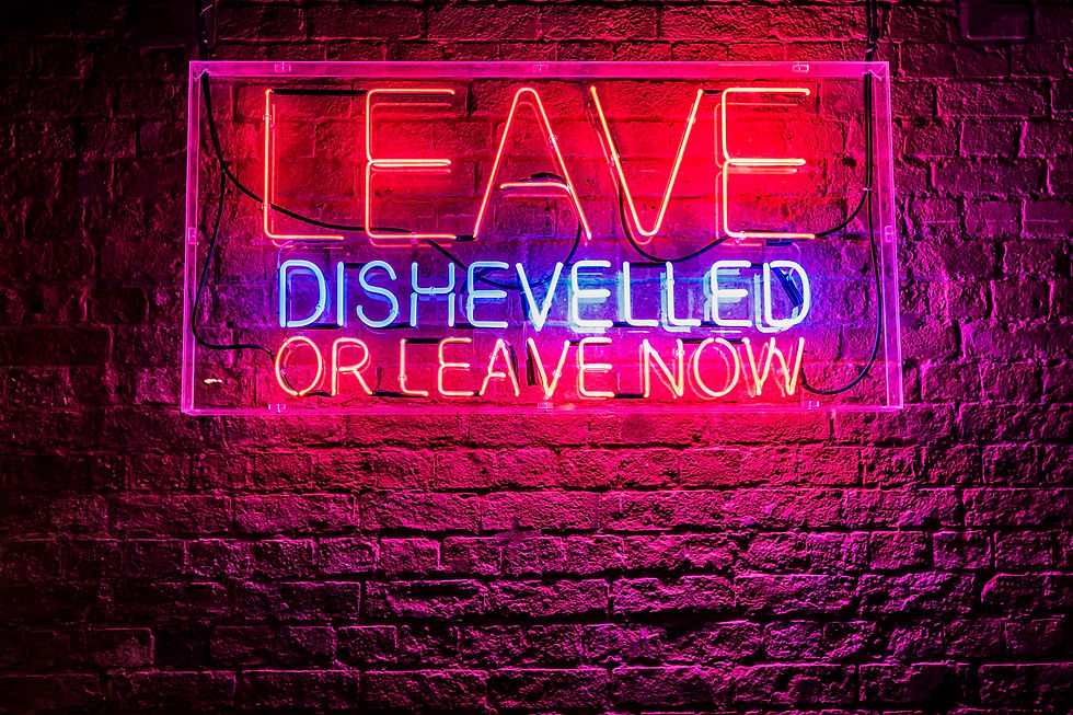Vibrant neon sign on a brick wall with the playful message: "Leave Dishevelled or Leave Now," creating a bold and whimsical atmosphere.