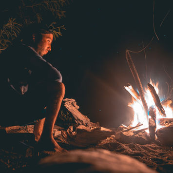 Man looking at a warm campfire in darkness