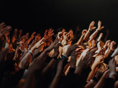 Dark, moody worship gathering with silhouetted hands raised in a crowded room, illuminated by dim stage lighting and haze, creating an atmosphere of intensity, emotion, and spiritual spectacle.