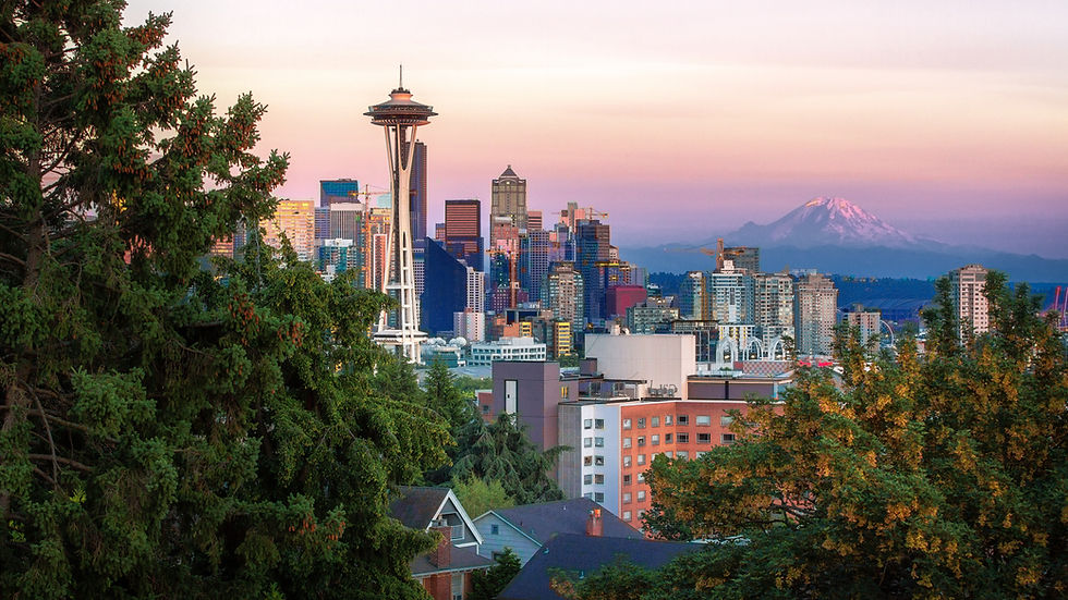 Seattle skyline with the Space Needle and Mt. Rainier at sunset, framed by green trees in the foreground.