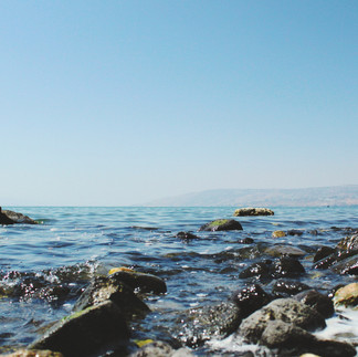 Crystal clear Close-up of gentle waves washing over ancient stones on a private tour of the Sea of Galilee. washing over black basalt stones on the peaceful shore of Lake Kinneret.