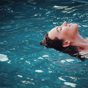 Woman in a colorful swimsuit floats peacefully on her back in a clear blue pool, eyes closed, enjoying a serene moment in the water.