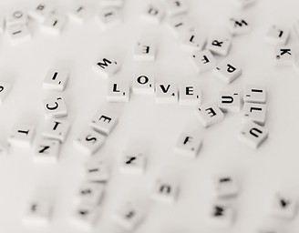 An image of Scrabble tiles spread out over a table. 4 letters in the middle of the image spell out the word "love"
