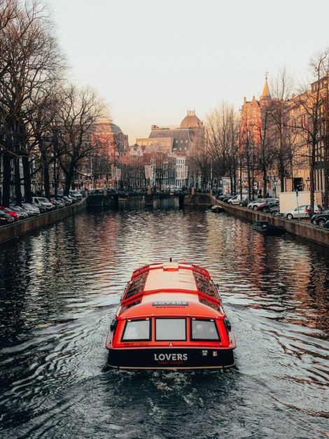 Red canal boat cruising through Amsterdam’s historic canals