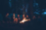 Men and women sitting around a campfire in a forest.