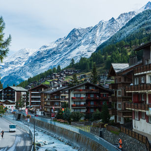A picturesque view of Zermatt, showcasing charming alpine chalets nestled against a backdrop of snow-capped mountains, with a serene river flowing through the village landscape.