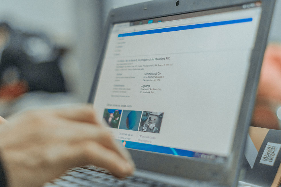 Hand typing on a laptop showing a blurred Portuguese news website, with a QR code card beside the screen.