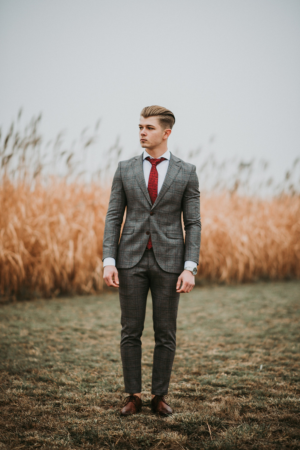 Man in a tight suit and red tie standing alone by a wheat field