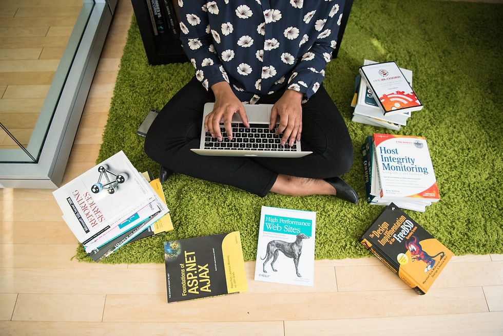 A woman dedicatedly upskilling, working on her laptop surrounded by a variety of technical and educational books.